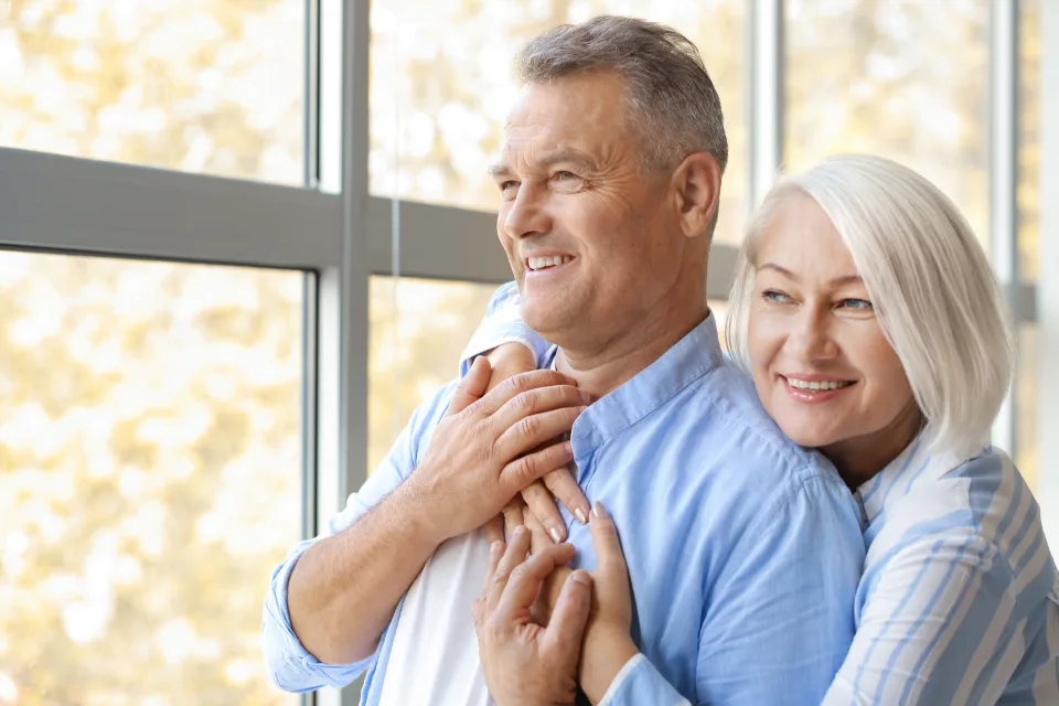 Older couple standing by a bright window at home